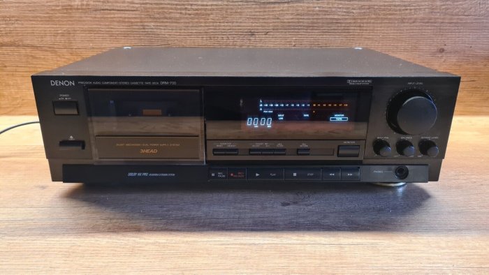 Svart Denon kassettbandspelare, DRM-700, digital display, reglage, knappar, på ett träbord.