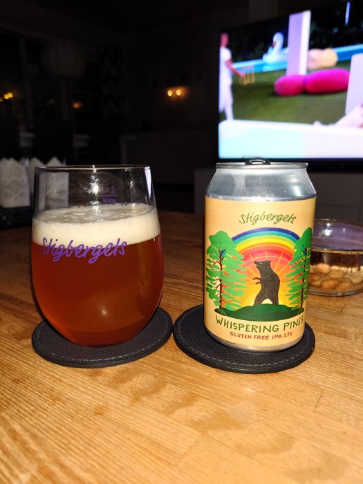 Ölglas och burk på bord, TV i bakgrunden, avslappnad hemmiljö.