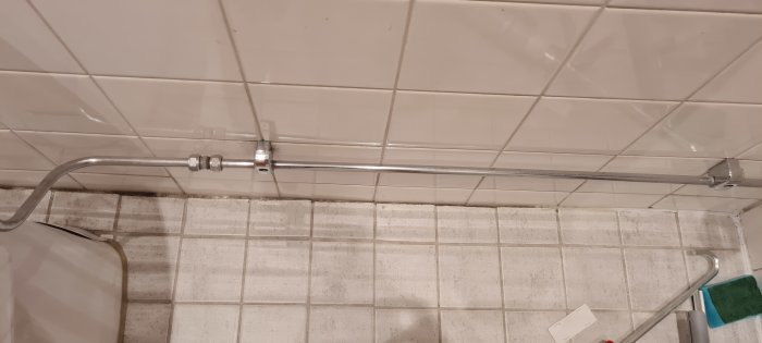 Metallrör på kakelvägg i badrum, gammal och smutsig tvättställskant synlig.