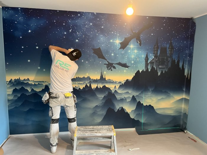 Arbetare applicerar fantasifull väggmålning i rum, drakar och slott, stjärnhimmel, berg.