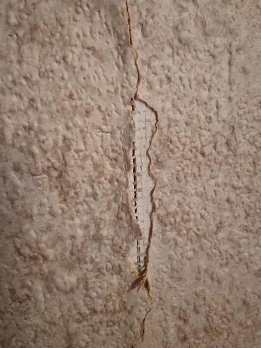 Vertikal spricka i en vit vägg visar inre lager och strukturell skada.