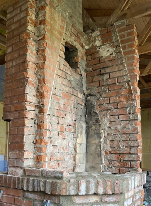 Förstörd tegelmursstruktur som en gång varit en skorsten, i ett tomt rum under renovering.