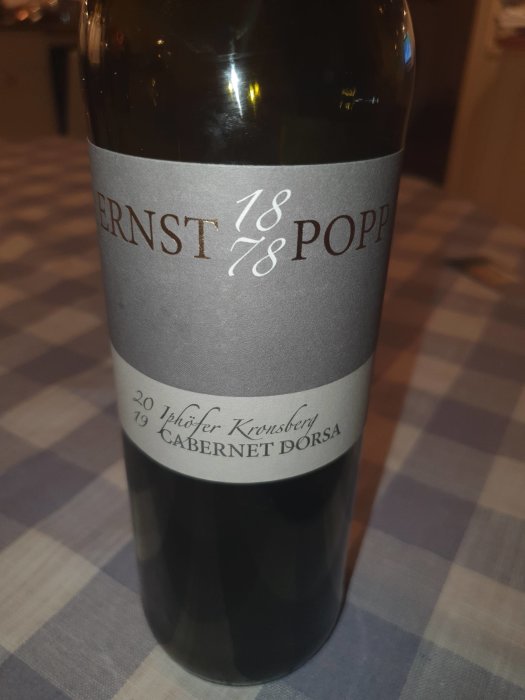 Flaska rödvin, "Ernst & Popp", "Iphöfer Kronsberg Cabernet Dorsa 2019", på rutig duk.