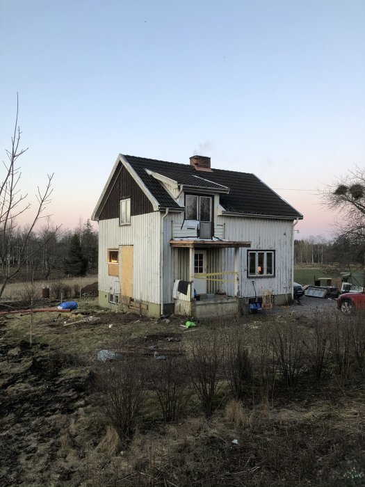 Ett slitet trähus med skorsten, leksaker utspridda, i skymningen, ödelagd trädgård, bostad ser bebodd ut.