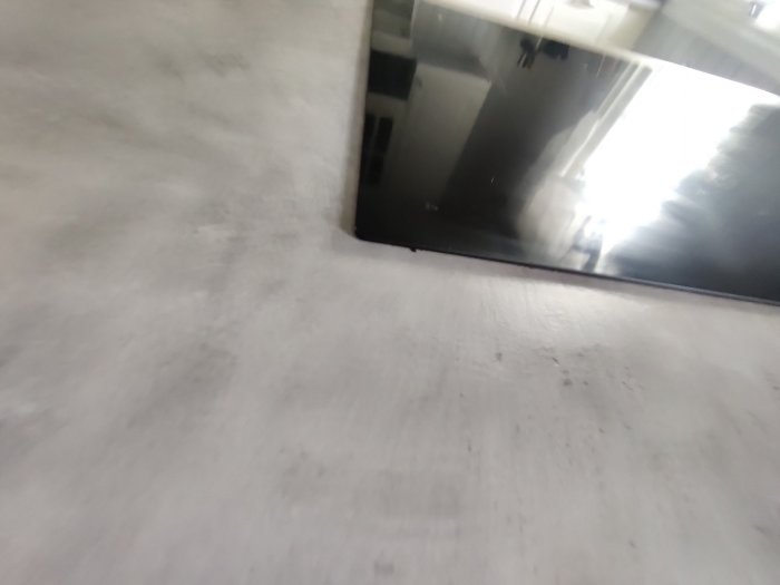 Oskarp bild, grå betongytor, svart rektangulärt objekt, reflektioner, belysning från höger, inomhusmiljö, arkitektoniska detaljer.