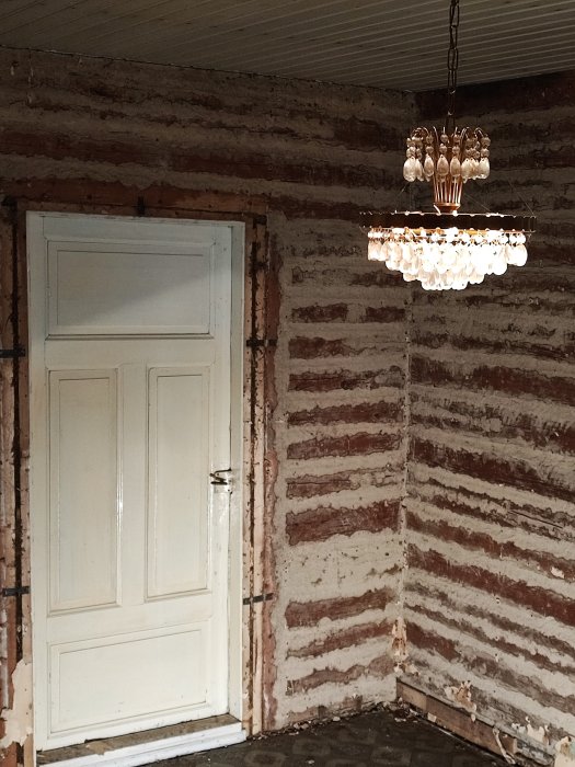 Renoveringsrum med nakna tegelväggar, elegant ljuskrona och stängd vit dörr.