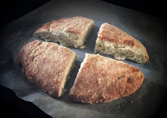 Fyra delar av nybakat bröd på bakplåtspapper, rustikt och hemgjort utseende, gyllenbrun skorpa.