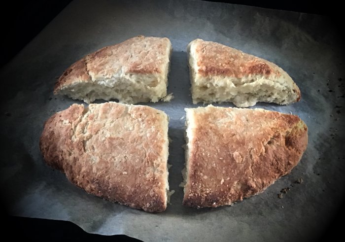 Fyra bitar av nybakat bröd på bakplåtspapper, gyllenbrunt, mjukt inuti, rustikt utseende.