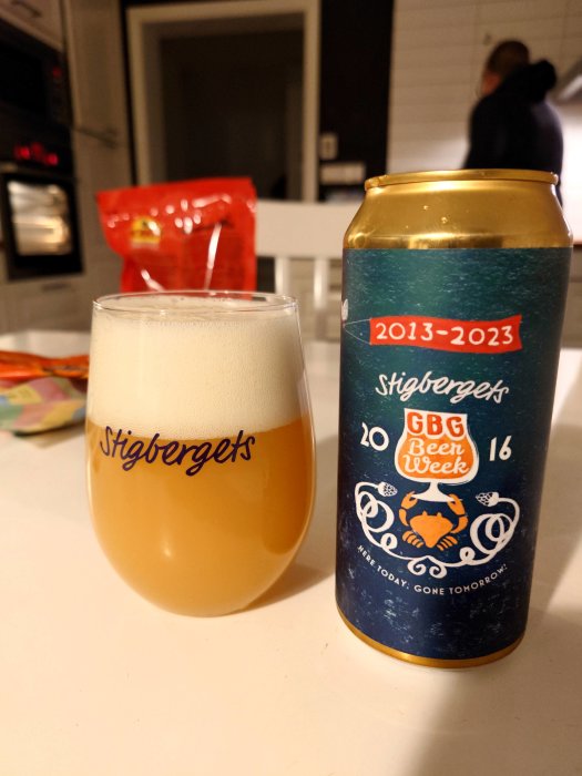 Ölglas med skum, Stigbergets ölburk, köksmiljö, person i bakgrunden.