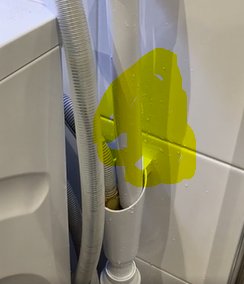 Duschhörna med vita kakel, genomskinlig duschslang och en gulfärgad fläck som täcker något i bilden.