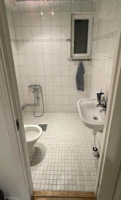 Ett litet badrum med dusch, toalett, handfat, kakel, och ett fönster.