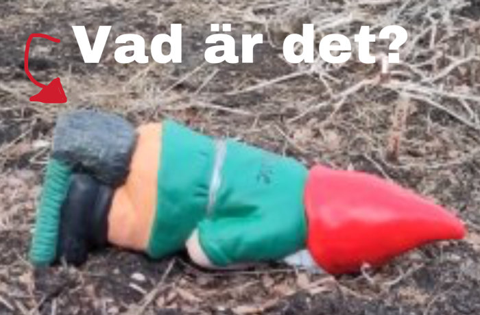 En leksakstomte ligger på marken, färgglad med röd mössa, text "Vad är det?" ovanför med en pil.