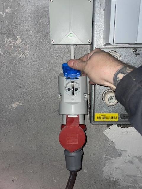 En hand ansluter en röd och blå industriströmkontakt till ett säkerhetskopplat vägguttag.