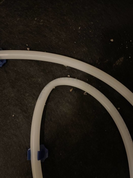 Två vita plastbågar med blå fästen på ett mörkt underlag. Smuts och småsten syns.