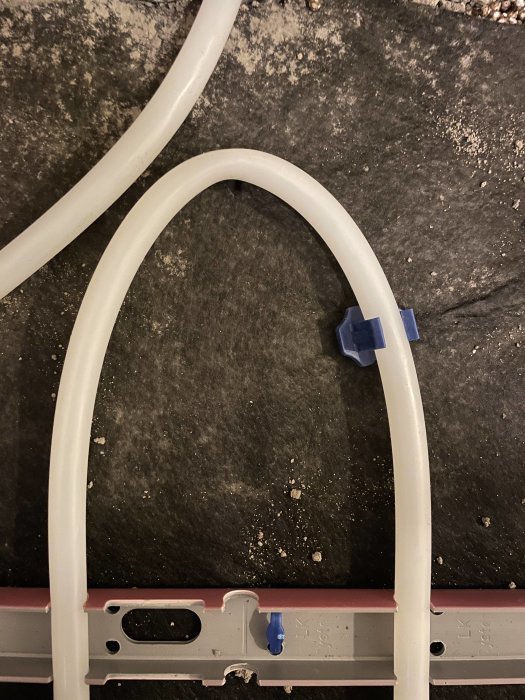 Vit plast, kurvig struktur, blåa klämmor, på mörk smutsig bakgrund, del av en större konstruktion.