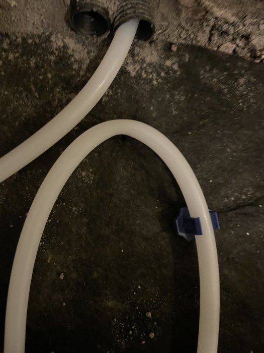 Två vita kablar och en svart sladdanslutning på en mörk, grov yta.