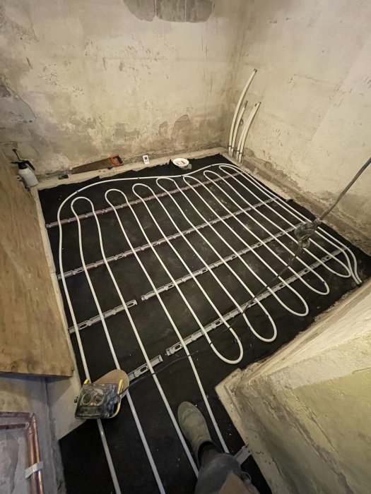 Installation av golvvärme, rör och klämmor på isolering, ofärdigt rum, verktyg, arbetsprocess.