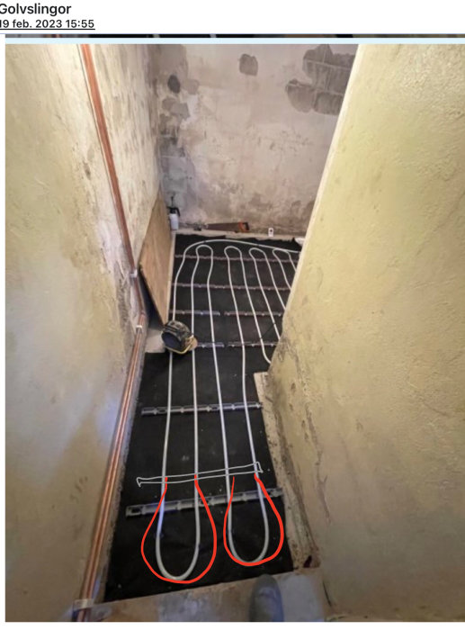 Installation av golvvärme i ett outrett rum med synliga rör och kabeldragningar på betonggolv.