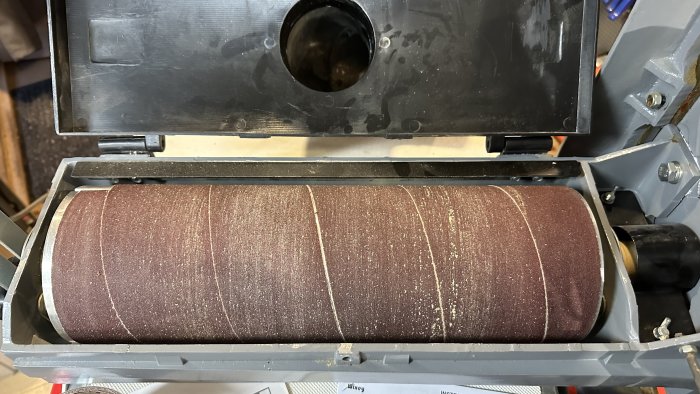 Sliprulle inuti en öppen slipmaskin, använd för att slipa material, med slitage och dammspår.