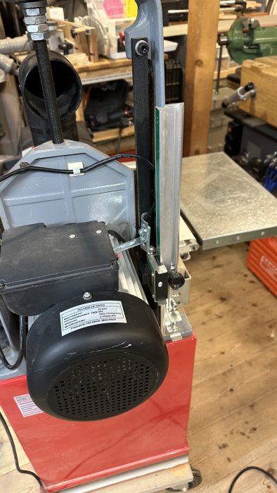 Verkstadsbandgåsåg på verktygsbänk med metallkonstruktion och motor, i en verkstadsmiljö.