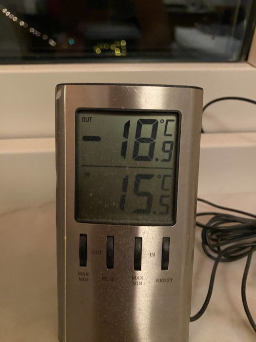 Termometer inomhus visar 15.5°C, utomhus -18.9°C. Knappar för max/min, återställning. Mörkt ute. Kabel syns.