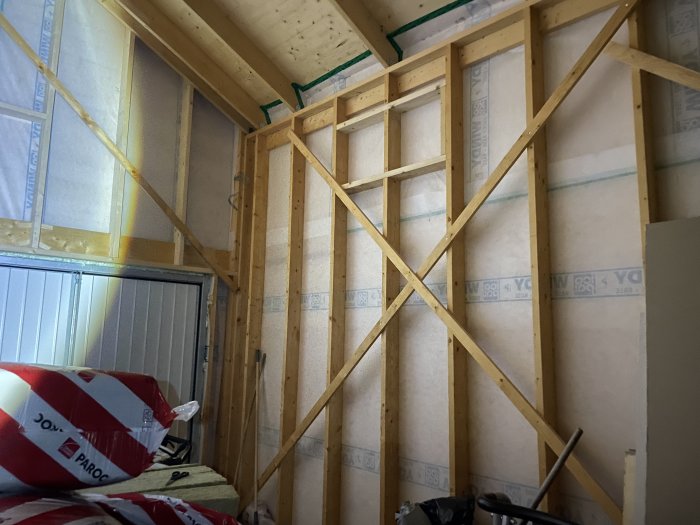 Inre stomme av trä i ett hus under konstruktion med isoleringsmaterial och byggmaterial synliga.