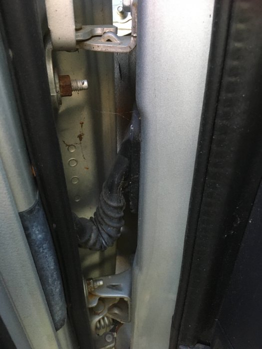 Närbild av fordonsdörr, mekaniska komponenter, ledningar, slitage, ingen människa synlig.