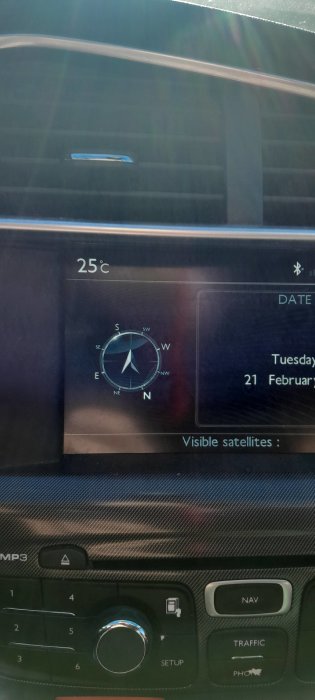 Bilens infotainmentsystem visar kompass, temperatur, datum och antal synliga satelliter. Solreflektioner syns.
