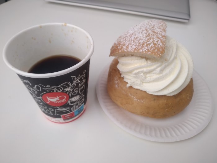 Pappersmugg med kaffe och en semla på tallrik, typiskt fikabröd, bakverk, svenskt.