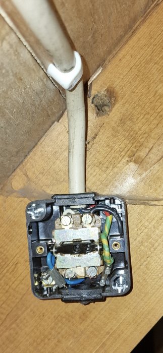 Öppen eluttagsdosa med exponerad ledningsanslutning och installationsfel, på en trävägg.
