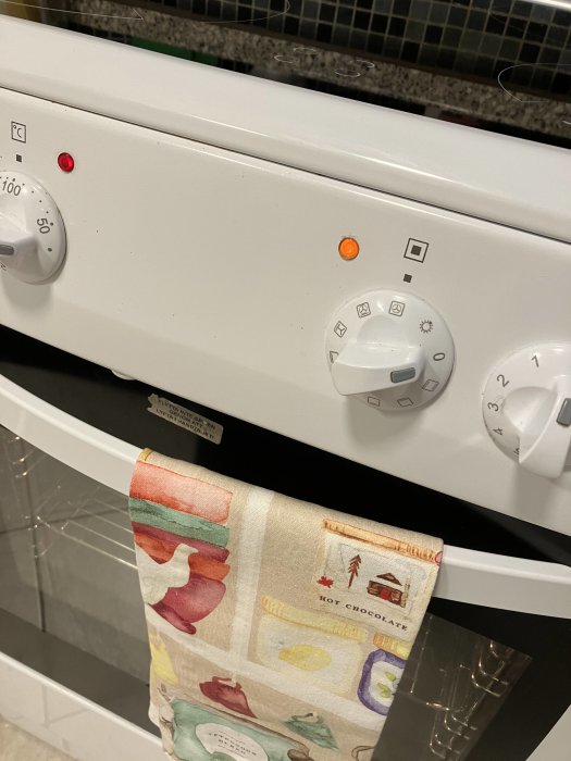 Vit diskmaskin framifrån, färgglad kökshandduk, kontrollknappar och indikatorlampor tända.