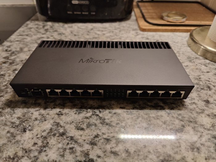 MikroTik-router med flera Ethernet-portar på köksbänk.