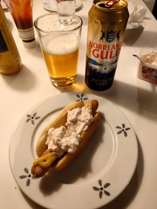 Korv med bröd, räksallad, senap. Ölglas och burk. Nordiskt tema. Matuppläggning på bord.