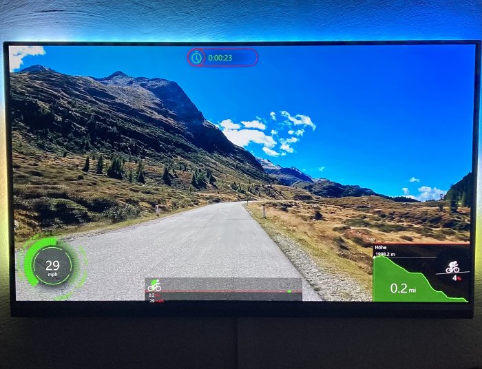 Tv-skärm visar en cykelsimulator med hastighetsmätare och bergslandskap.