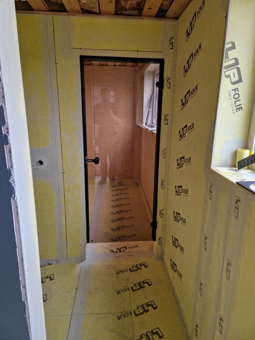 Oavslutad korridor, isolering synlig, spegelbild av en person, trä och isoleringsmaterial, byggarbetsplats eller renovering.