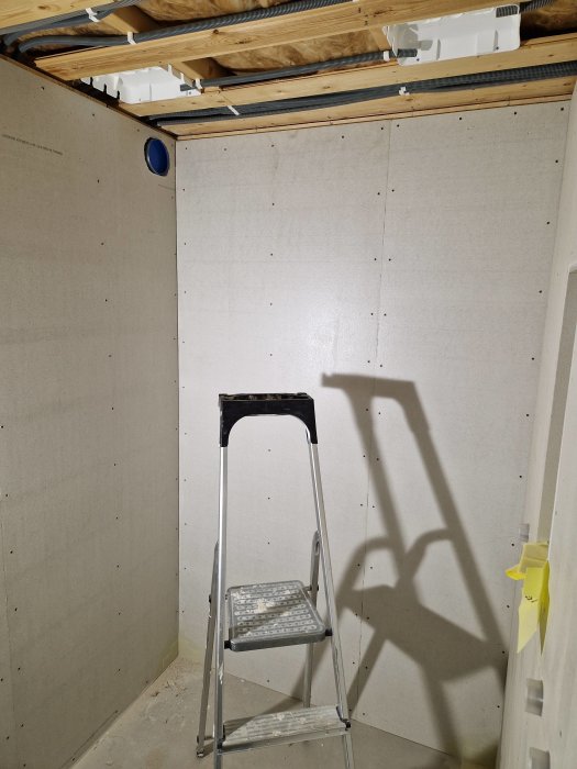 En stege i ett rum under konstruktion med gipsskivor och odraget eluttag.