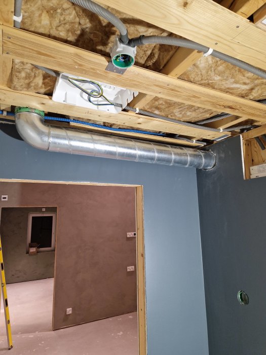 Byggplats med öppet tak, isolering, elinstallationer, ventilationsrör och delvis färdiga väggar.