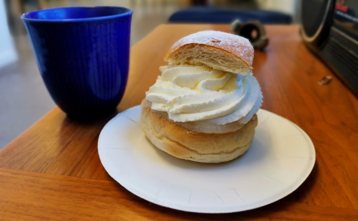 Semit med grädde på tallrik, blå kopp, bakgrund suddig, närbild, fika, träbord.