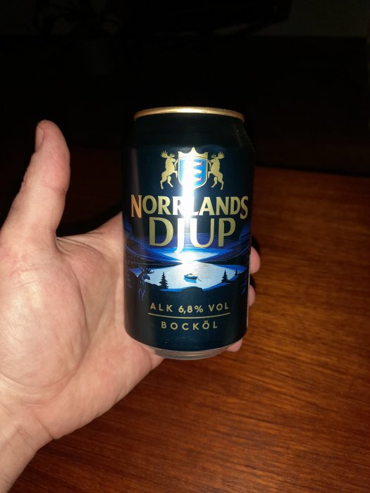 Hand håller ölburk, "Norrlands", skoglandskap, alkoholhalt 6,8%, mörk bakgrund.