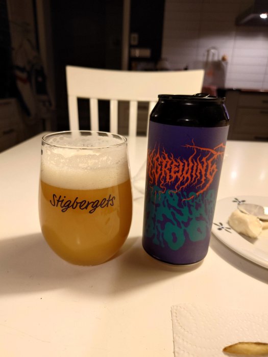 Ölglas med skum, ölburk med mönster, vitt köksbord, stol, tallrik med snacks.