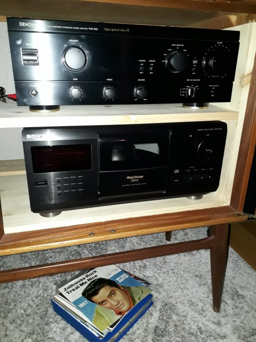 Stereoanläggning med förstärkare och CD-växlare på hylla, Elvis Presley skivomslag på golvet.