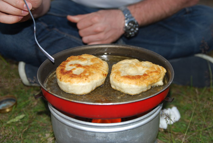 Stekning av bullar på portabelt kök ute, person sitter bredvid med gaffel.