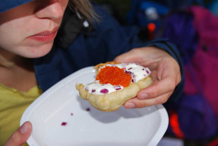 Kvinna håller i tunnbröd med gräddfil, lök och röd löjrom på vitt fat.