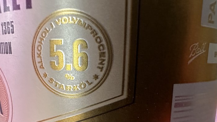 Fotografi av etikett med alkoholvolymprocent på 5,6%, glänsande yta, detaljer i guld, indikerar stark dryck.
