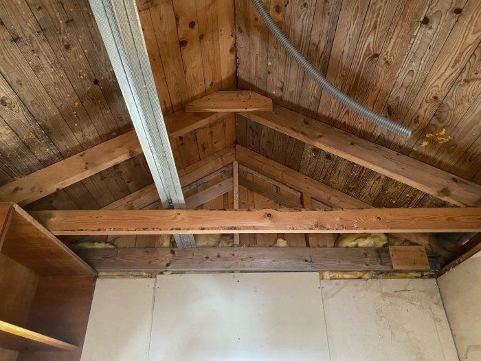 Träbjälklag med isolering sedd från nedan, lutande takkonstruktion, synlig ventilationsslang.