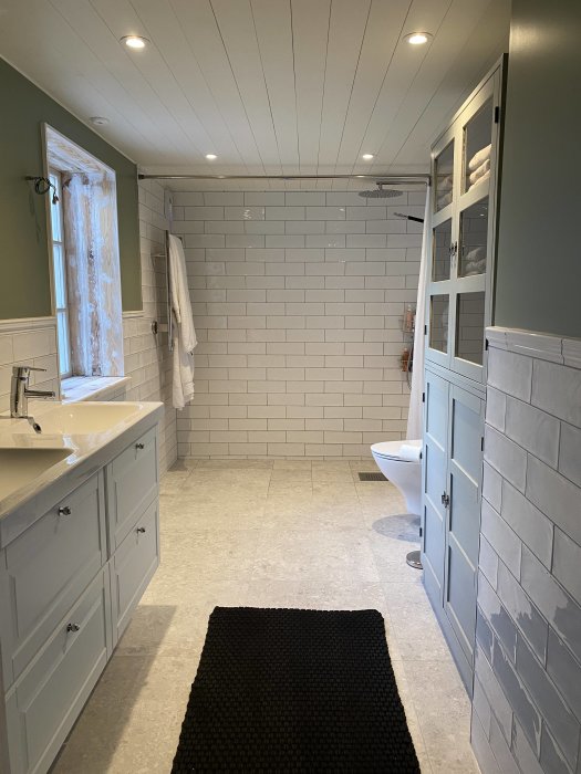 Ett modernt badrum med grå skåp, kakelväggar, dusch och inbyggd belysning.