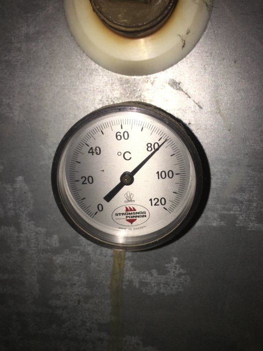 Termometer som visar cirka 75 grader Celsius, monterat på vägg, betecknad "STRÖMSNÄS PANNAN", "MADE IN SWEDEN".
