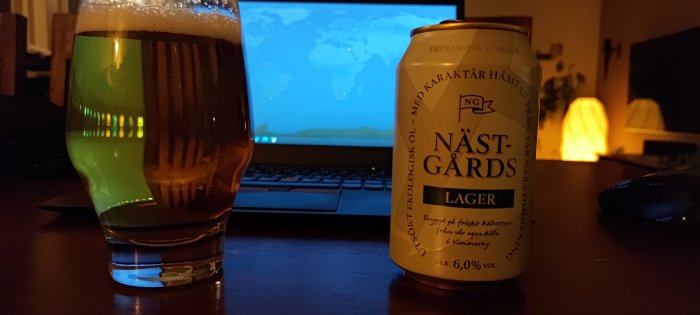Ett ölglas, burk med text "NÄSTGÅRDS Lager", laptop, mysig belysning, hemmiljö, avslappnat.