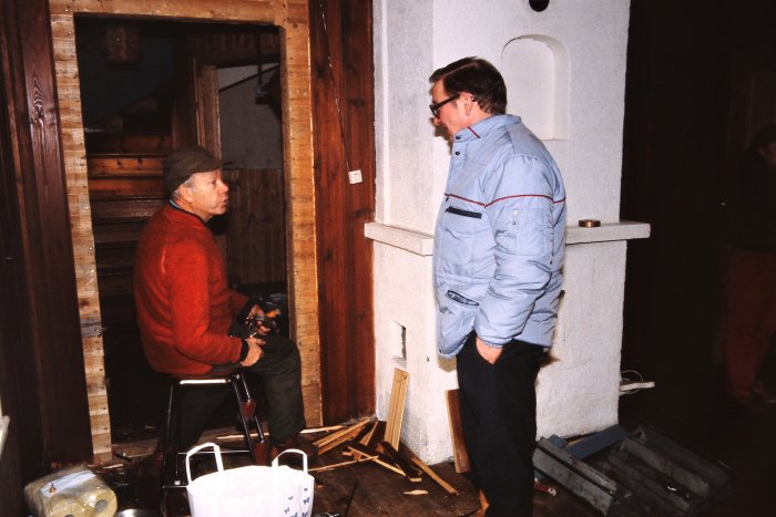 Två män i ett rum med träväggar, en sittande med kamera, den andra står.