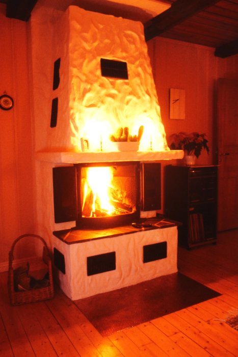 En mysig eldstad med öppen spis brinner i ett hemtrevligt rum med trägolv och korg.